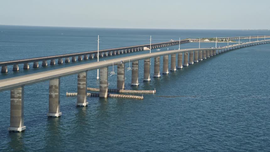 Ascending next to Seven Mile Bridge in Florida this aerial footage captures the approach of vehicles as they travel over the bridge in the bright sunshine