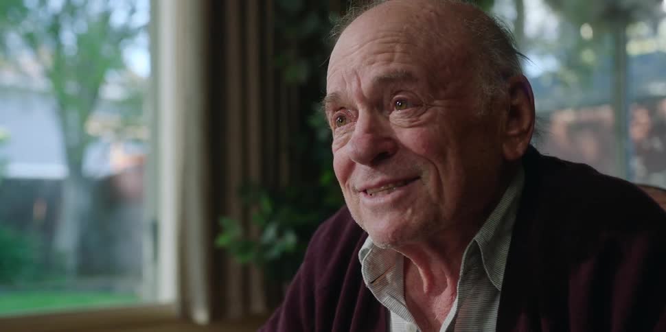 An elderly man at home smiles as he talks