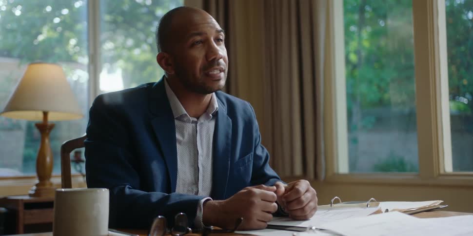 A man sitting behind a desk discusses information with another person