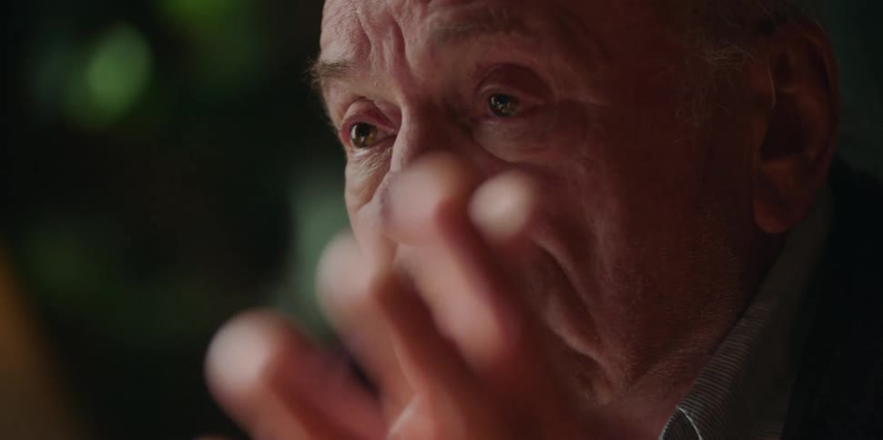A man gestures toward himself while speaking