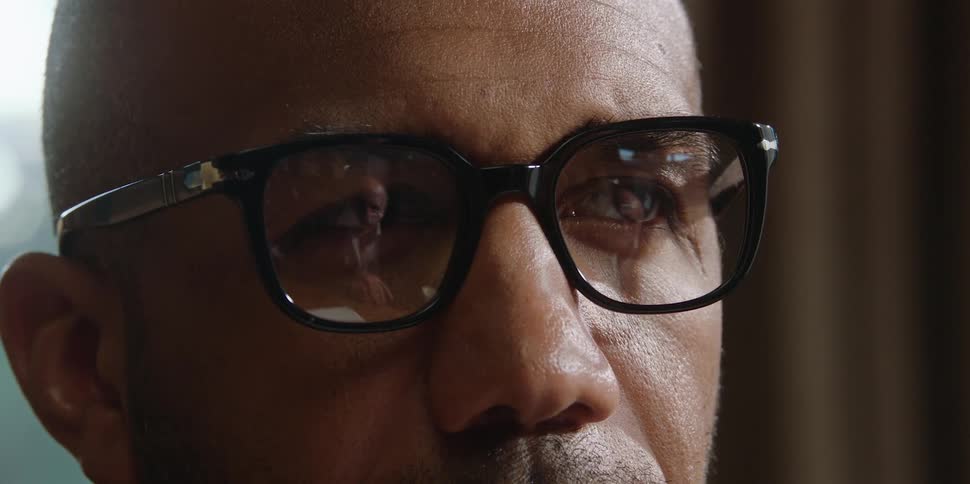 A black man having a conversation with an elderly white man whose reflection is visible in the first mans glasses