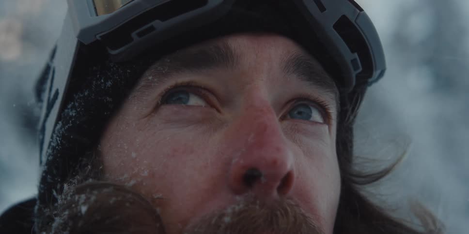 A man wearing goggles on his head looks up at the falling snow