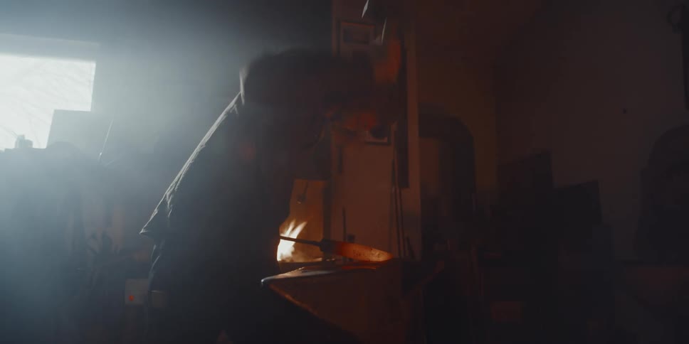 Male blacksmith in workshop shaping a piece of metal with a hammer during the day