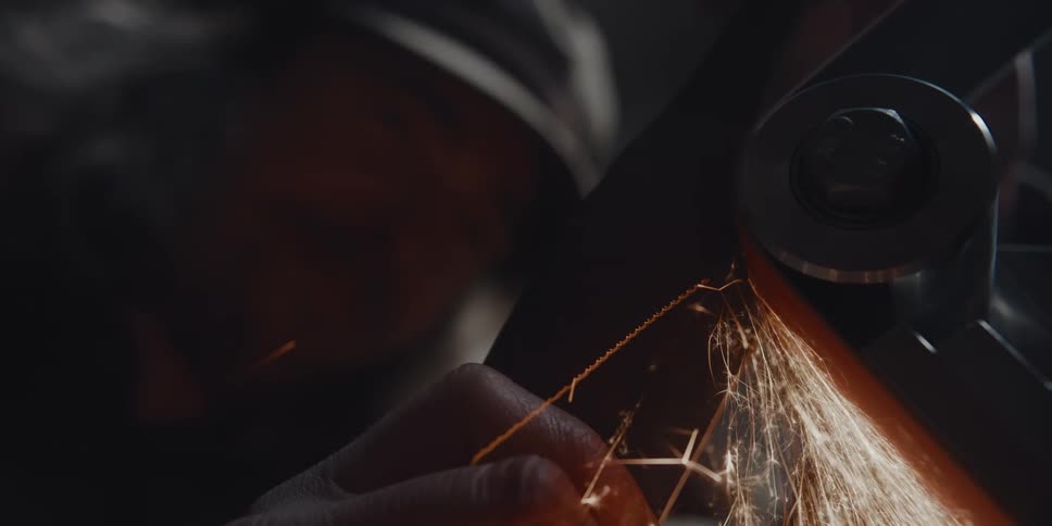A person grinding metal on a belt grinder