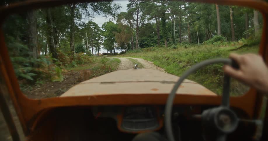 A person is driving an oldsteering vehicle through a wooded area