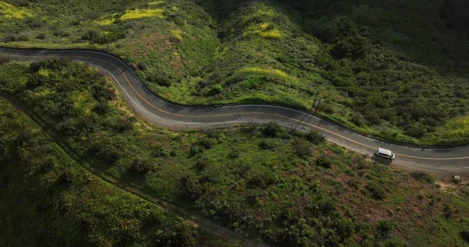 Aerial view of vehicles driving on winding road in the field