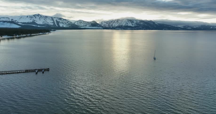 A sailboat sails along the snowy coastline passing a pier