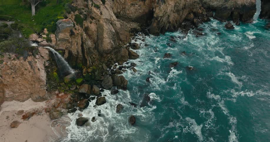 Waterfall flowing into a rocky beach with blue waves