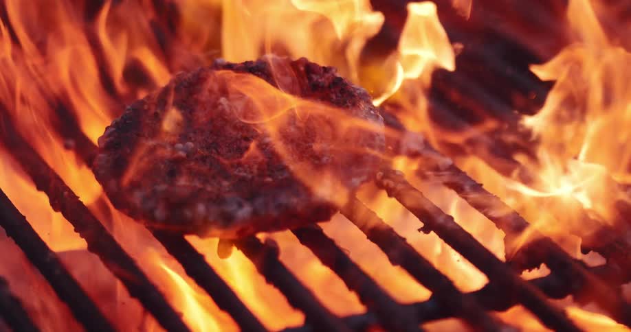 A burger being flipped on a grill with flames