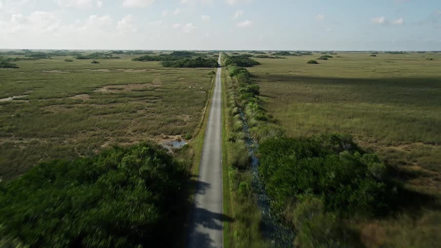 Driving along a scenic country road in Floridas Everglades passing marshes and landmarks with partly cloudy skies above