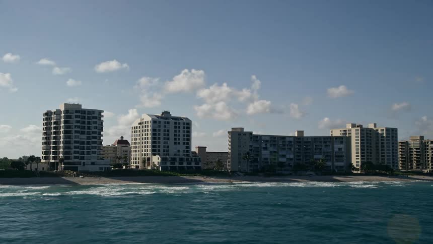 A stunning aerial view of condominium complexes on the beach in Highland Beach Florida with people enjoying recreational activities along the shoreline on a partly cloudy day
