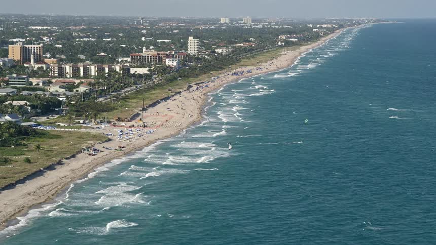 A stunning aerial view of kite surfers gliding over the waves near a beach in Delray Beach Florida during a partly cloudy day