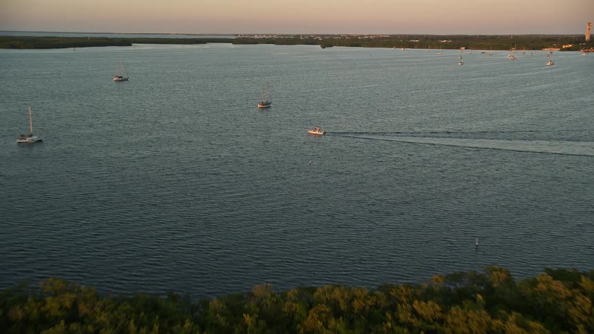 As the sun sets in Key Largo the video shows an aerial view flying over mangroves to approach fishing and sailboats capturing the beautiful scenery of recreational activities on the water