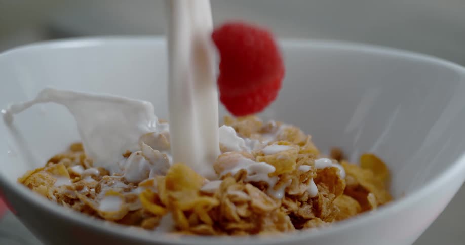 Milk and raspberries being poured into a bowl of cereal