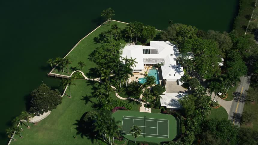 Flying over a luxurious mansion with a pool tennis court and waterfront view in Coral Gables Florida