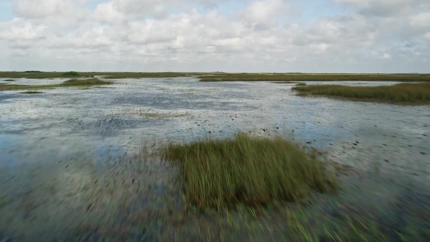 Flying low over the wet marshland of Florida Everglades revealing sloughs and natural landmarks on a partly cloudy day