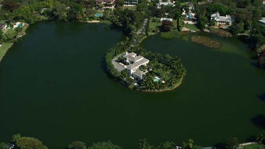 Aerial view of a mansion on an island in Hammock Lake Coral Gables Florida tilting down to showcase the shoreline and waterfront property