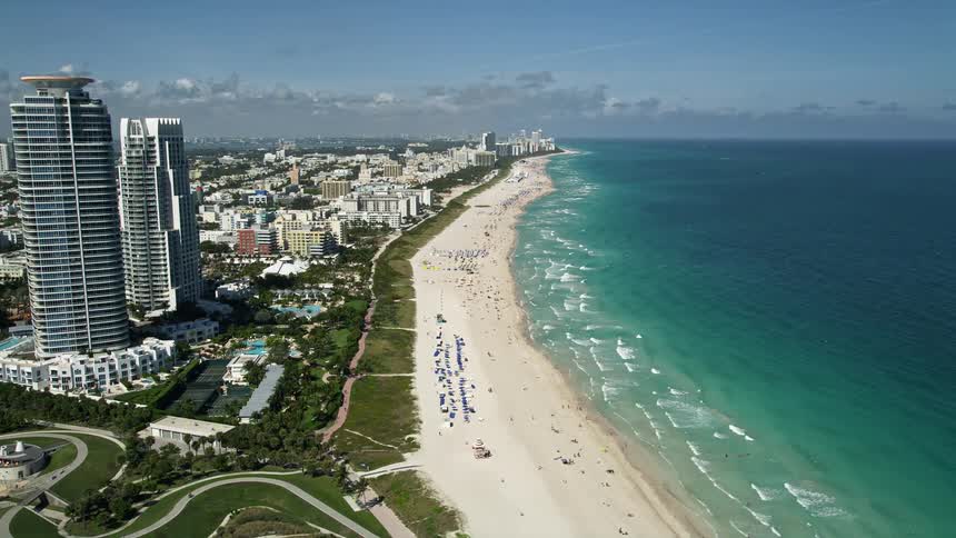 Aerial footage of South Beach Miami Beach Florida shows a large crowd enjoying a sunny day on the beach with high rise towers visible in the background