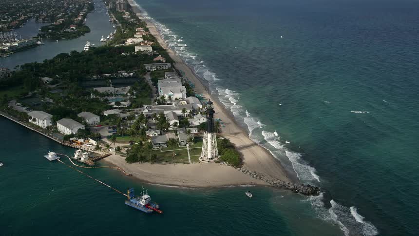 Approaching the famous Hillsboro Inlet Light this 5K aerial footage tilts down to reveal sunbathers and beach-goers enjoying the day on Hillsboro Beach Florida