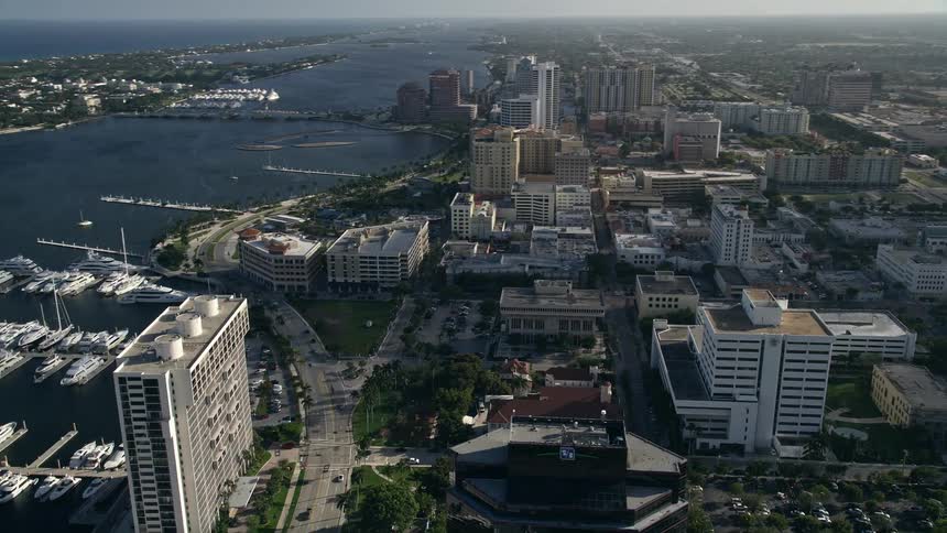 Panning aerial view above office buildings revealing a marina with boats docked in West Palm Beach FL