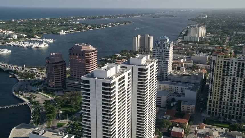 Aerial view of approaching Trump Plaza in West Palm Beach Florida with tall buildings and residences visible along the waterfront during the day