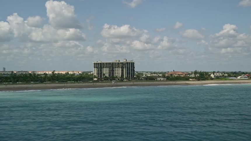 Flying over a beachfront apartment building in Fort Pierce Florida with a view of the ocean and populated beach on a partly cloudy day