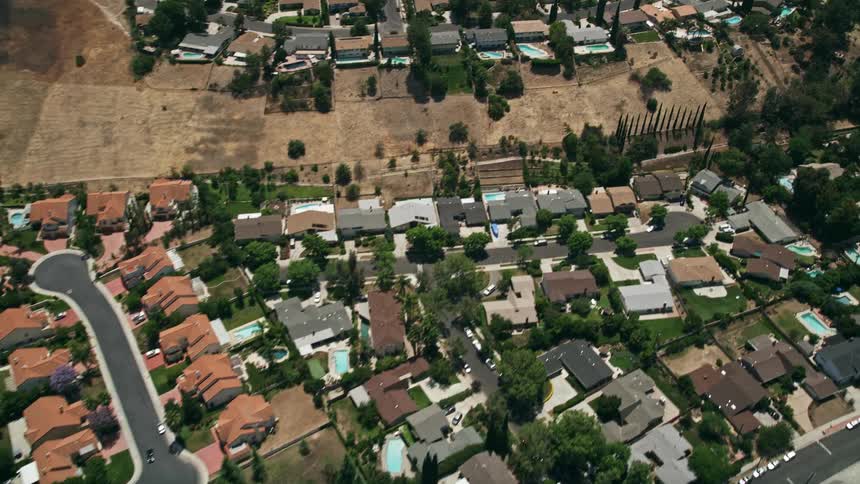 A stunning reverse aerial shot of beautiful tract homes with swimming pools set amidst the sunny and peaceful suburbs of Calabasas California