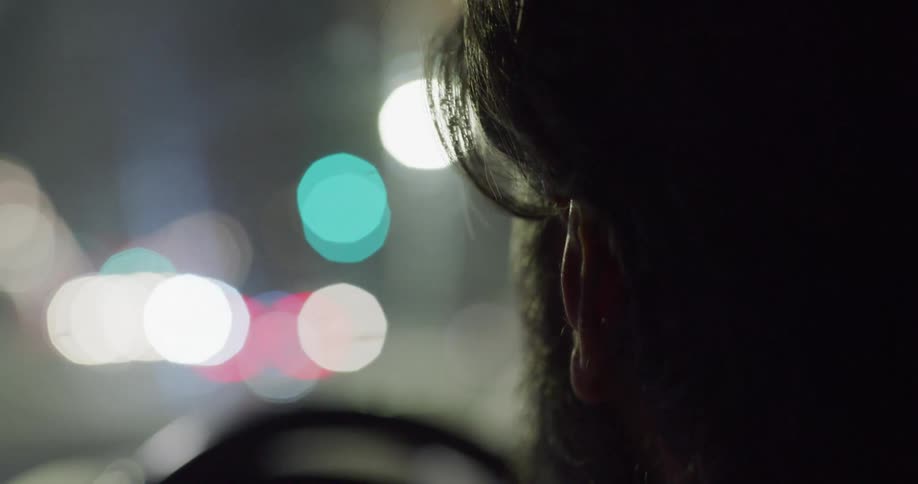 A side profile of a mans face with a beard as he drives his vehicle at night