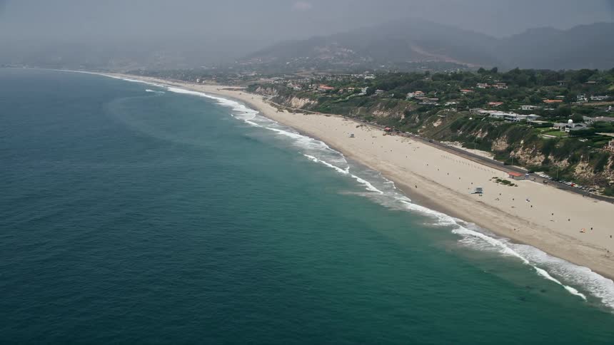 An aerial view of a sparsely populated beach in Malibu California with a view of the Pacific Ocean and the mountain range in the distance