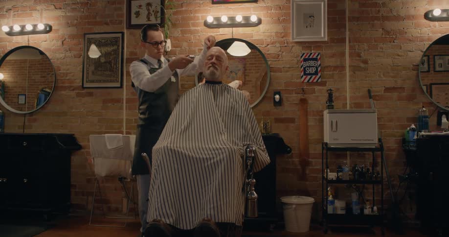 A barber carefully trims an older mans side hair in a barber shop