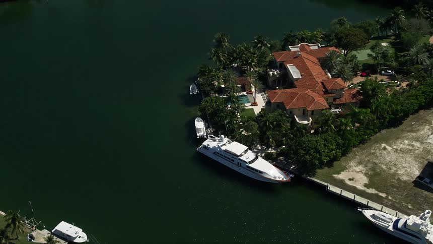 Aerial footage of a mansion in Coral Gables Florida with a yacht docked in front on a sunny day
