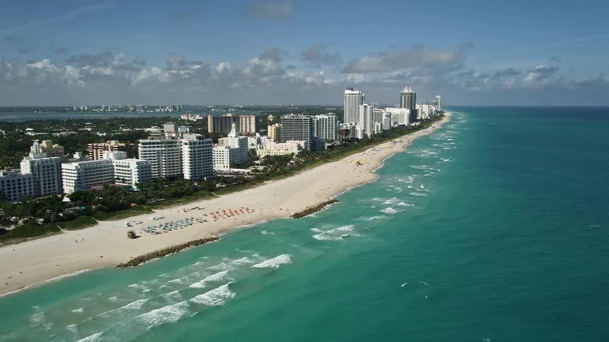 A stunning aerial view of Miami Beach shoreline and resorts with people enjoying the beach during daytime under the sunny clear sky captured in 5K Florida Aerials shoot