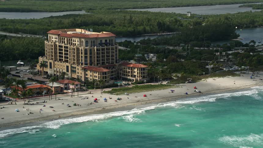 An aerial view of The Villas of Positano a residential condominium building in Hollywood Florida located by the beach on a partly cloudy day with people enjoying leisure activities such as sightseeing and sunbathing