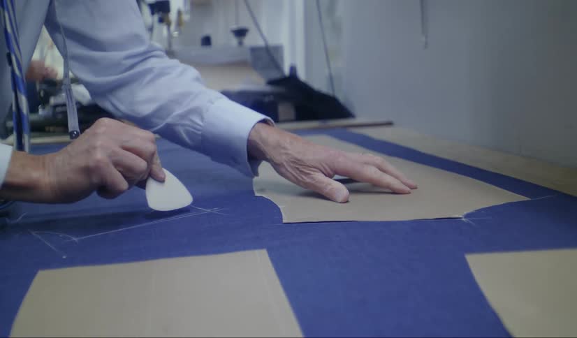 A clothing maker uses chalk to trace a shape on fabric
