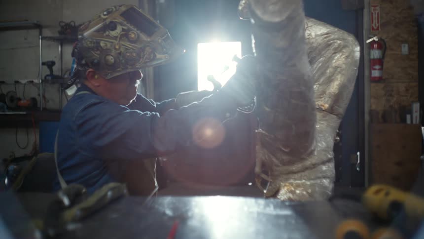 A metal sculptor hammers and chisels a piece of metal
