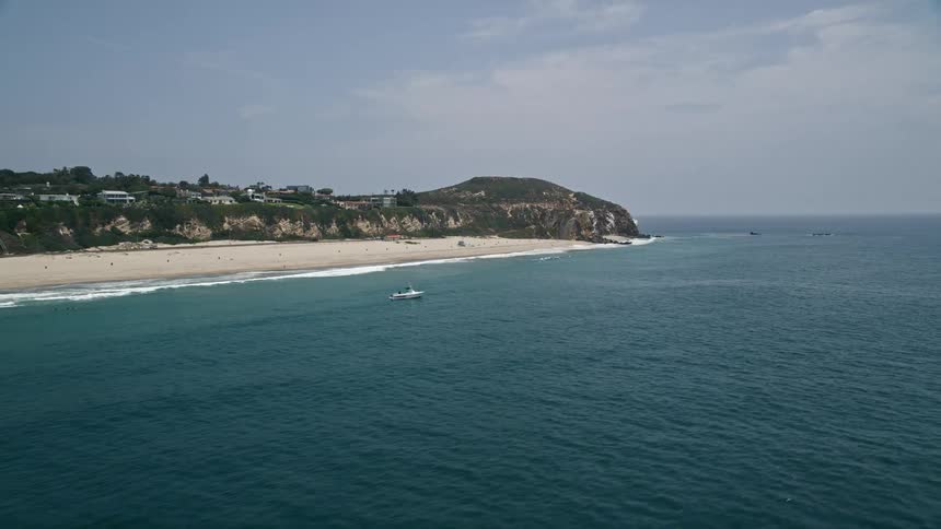 An aerial view of a sparsely populated beach and Point Dume in Malibu California with a sandy beach beneath a towering coastal cliff perfect for seaside recreation and leisure activities in the spring or summer