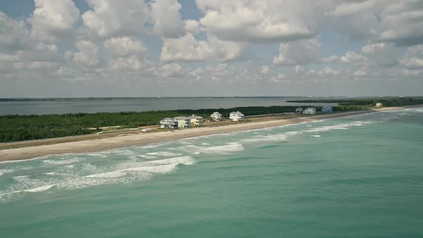 Aerial footage of beachfront homes and neighborhoods along the shoreline of Fort Pierce Florida with partly cloudy skies and blue ocean waters