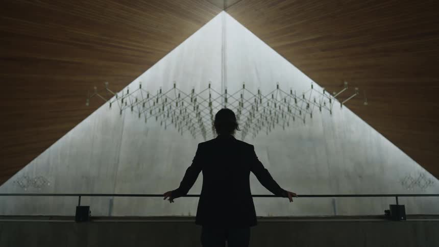 The silhouette of a man in church in a suit walking up to a railing placing his hands on it and looking out over it