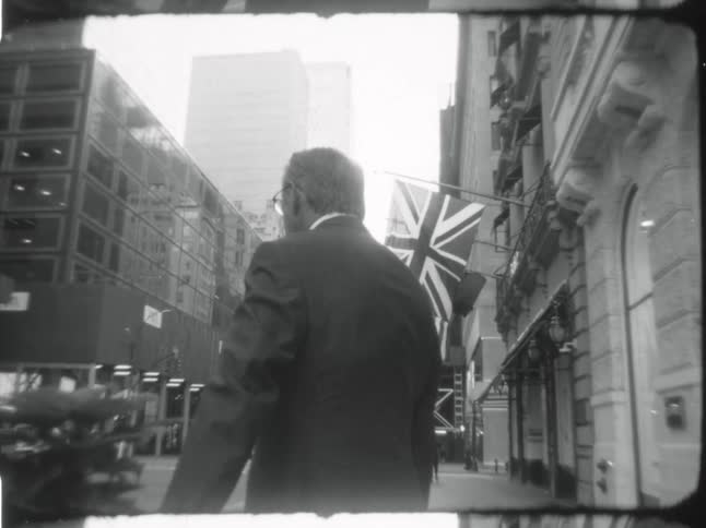 Man wearing a business suit stands outside a building in the city caught on vintage film