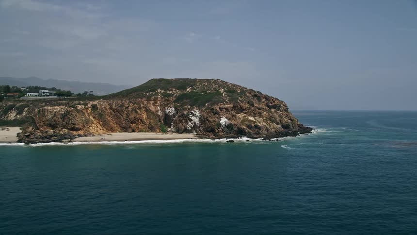 An aerial footage of a sparsely populated beach and Point Dume in Malibu California with waves crashing against the shore