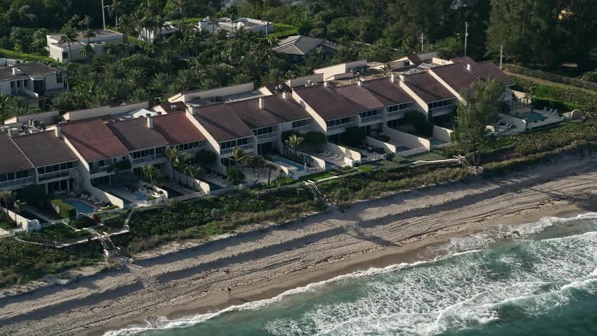 Aerial footage of passing condominiums by the beach in Palm Beach Florida with sunny skies and beachgoers
