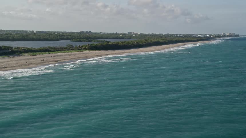 A breathtaking aerial view of John D MacArthur Beach State Park in Riviera Beach Florida showcasing the sandy beaches and clear waters of the Florida coastline on a partly cloudy day