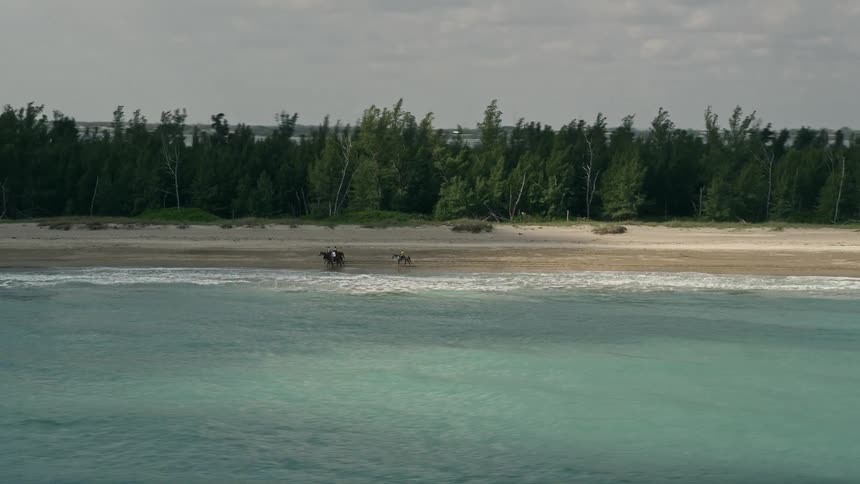 Horseback riders enjoy tracking along the shoreline of the blue waters and sandy beaches of Fort Pierce Florida in this 5K aerial stock footage