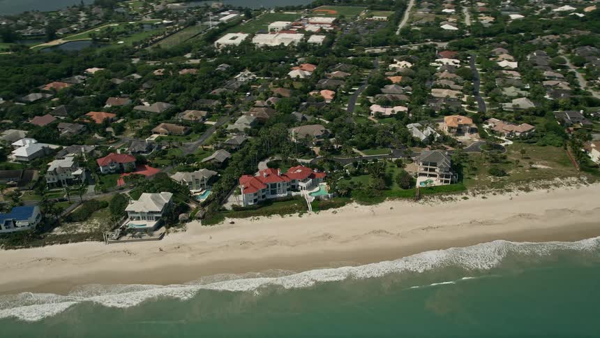 Aerial footage of an upscale residential beach neighborhood in Vero Beach Florida with mansions and luxury homes on display captured during a partly cloudy summer day