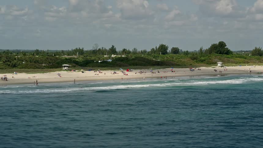 Aerial footage of sunbathers and beach-goers enjoying a partly cloudy day on the shores of Fort Pierce Florida during summer