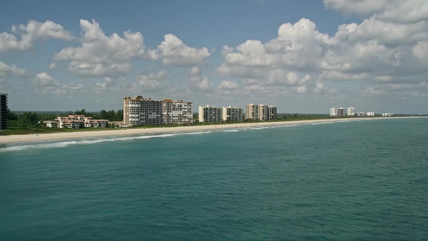 An aerial flyby of beachfront apartment buildings on the coastline of Fort Pierce Florida with partially cloudy skies during the day
