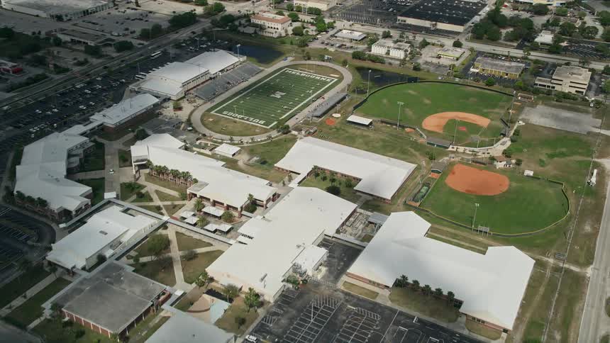 Approaching aerial view of a high school with sports fields in Melbourne Florida on a partly cloudy day