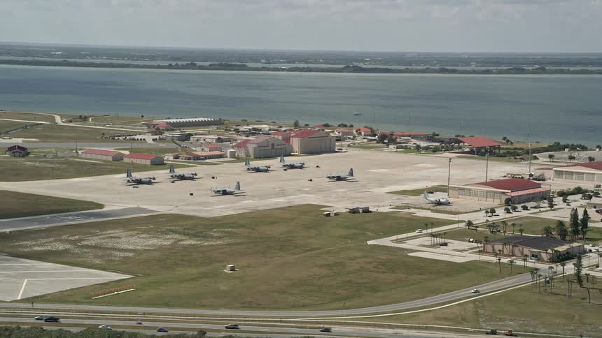 Footage of parked turboprop military planes at Patrick Air Force Base in Florida by the coast with partly cloudy skies and a nearby highway during daytime