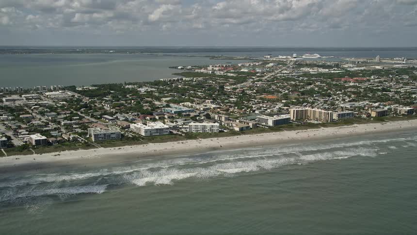 An aerial view of a populated beach with hotels and condominiums lining the shore situated in Cocoa Beach Florida under partly cloudy skies