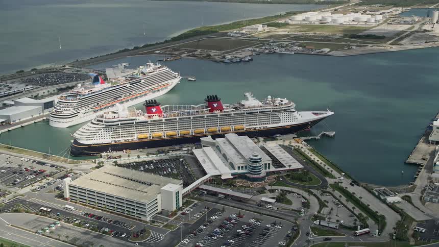 Aerial footage of Disney and Carnival Cruise ships orbiting Port Canaveral Florida on a partly cloudy day during vacation season